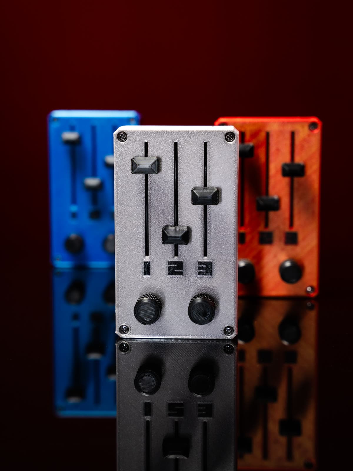 KNOB plateado de frente, con las versiones azul y cobriza desenfocadas atrás, sobre fondo rojo oscuro con reflejo